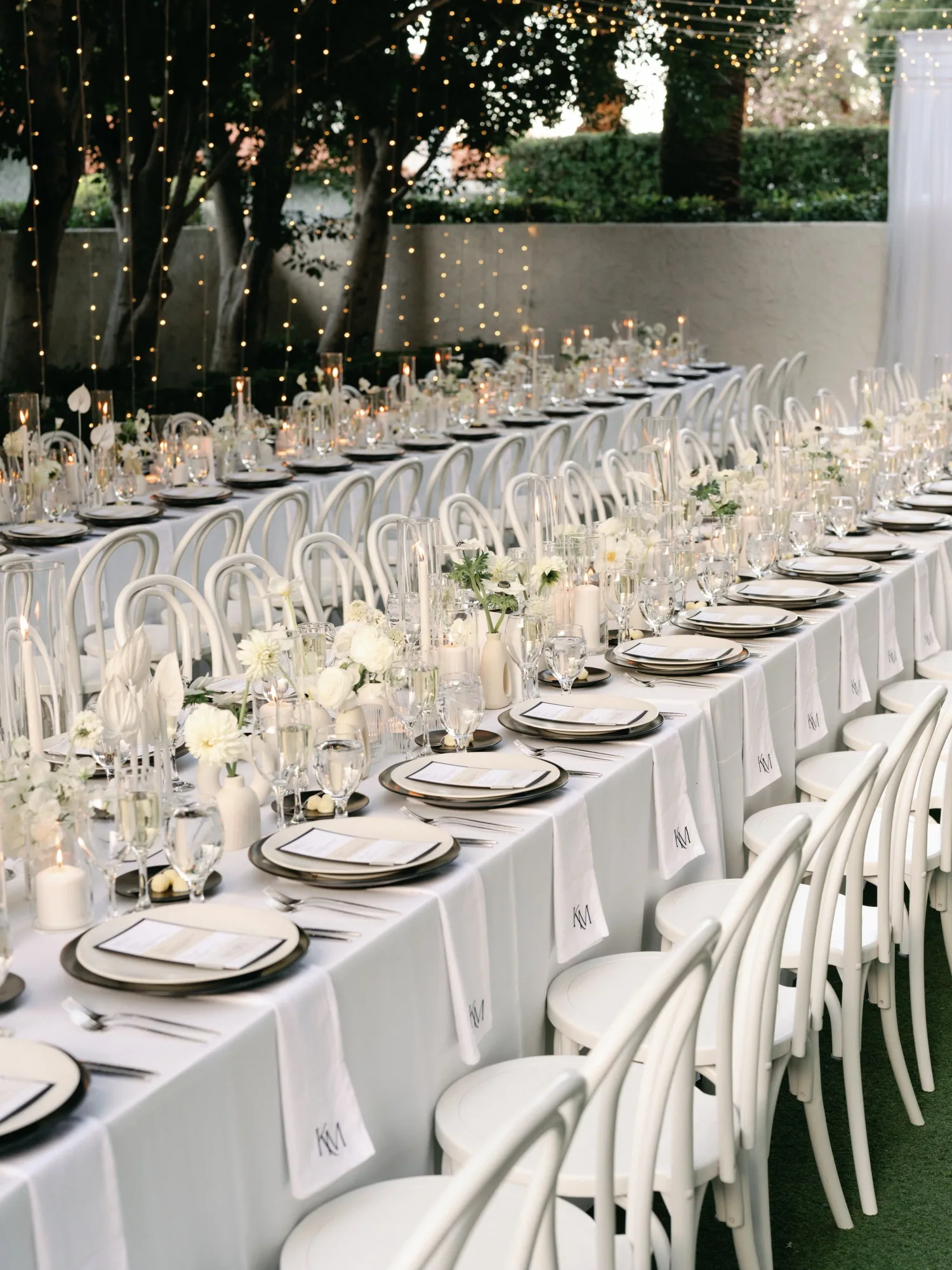 A long candlelit dinner table set beneath hanging lights.