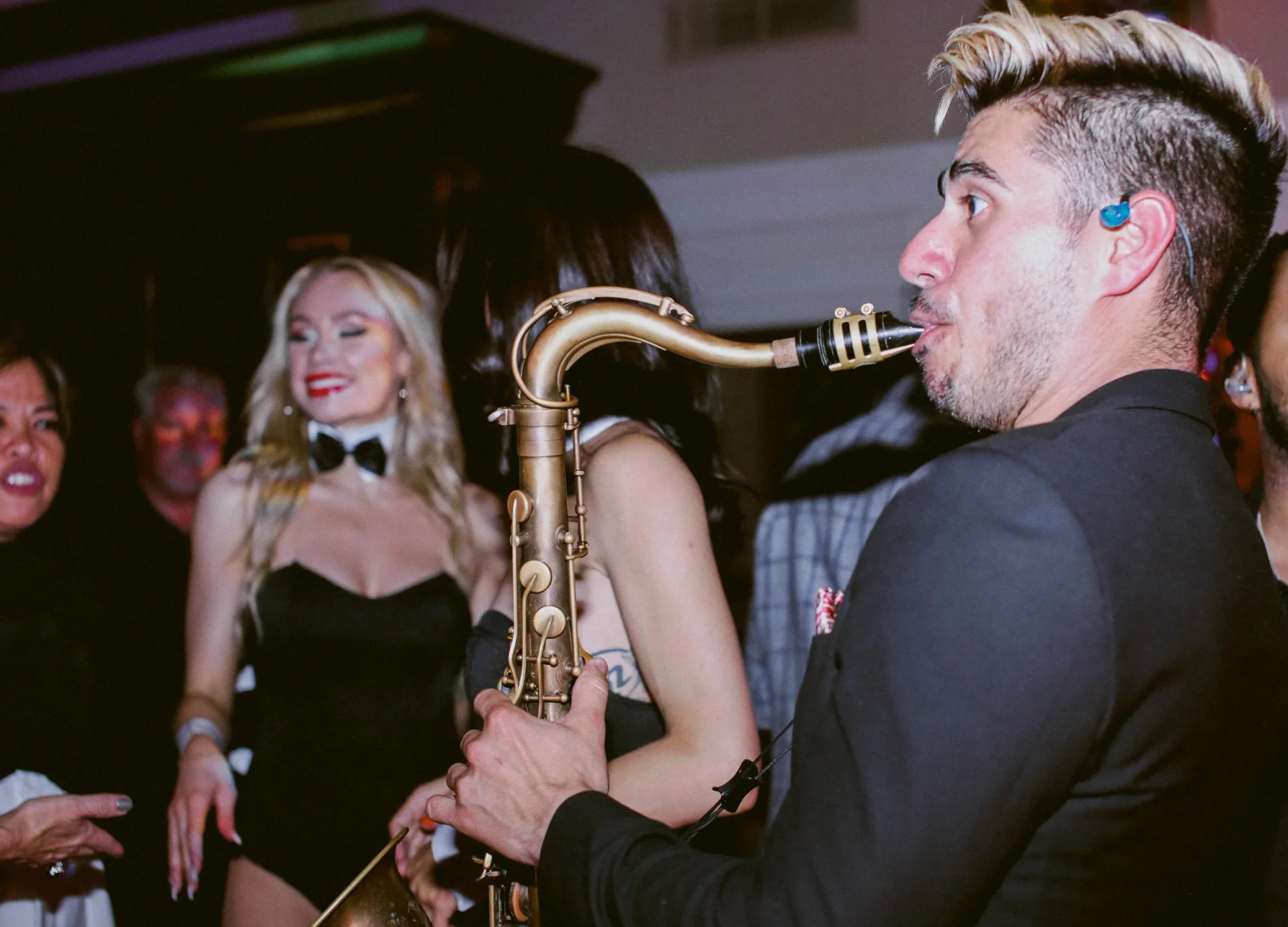 A DJ Live saxophonist performing in the center of a crowded dance floor.