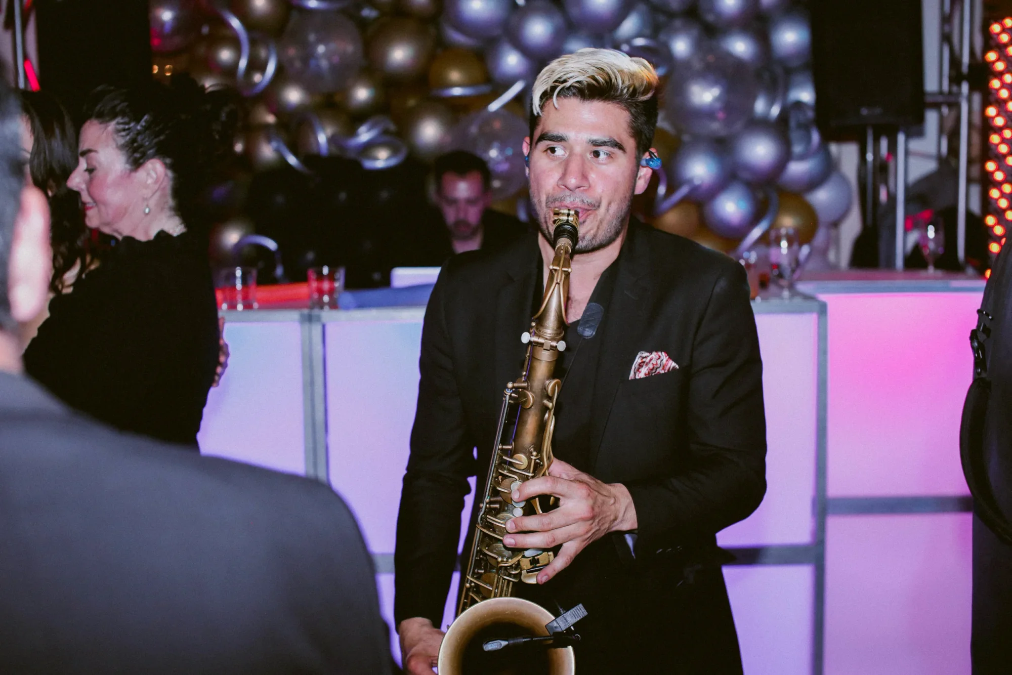 The DJ Live saxophonist playing beside the illuminated booth.