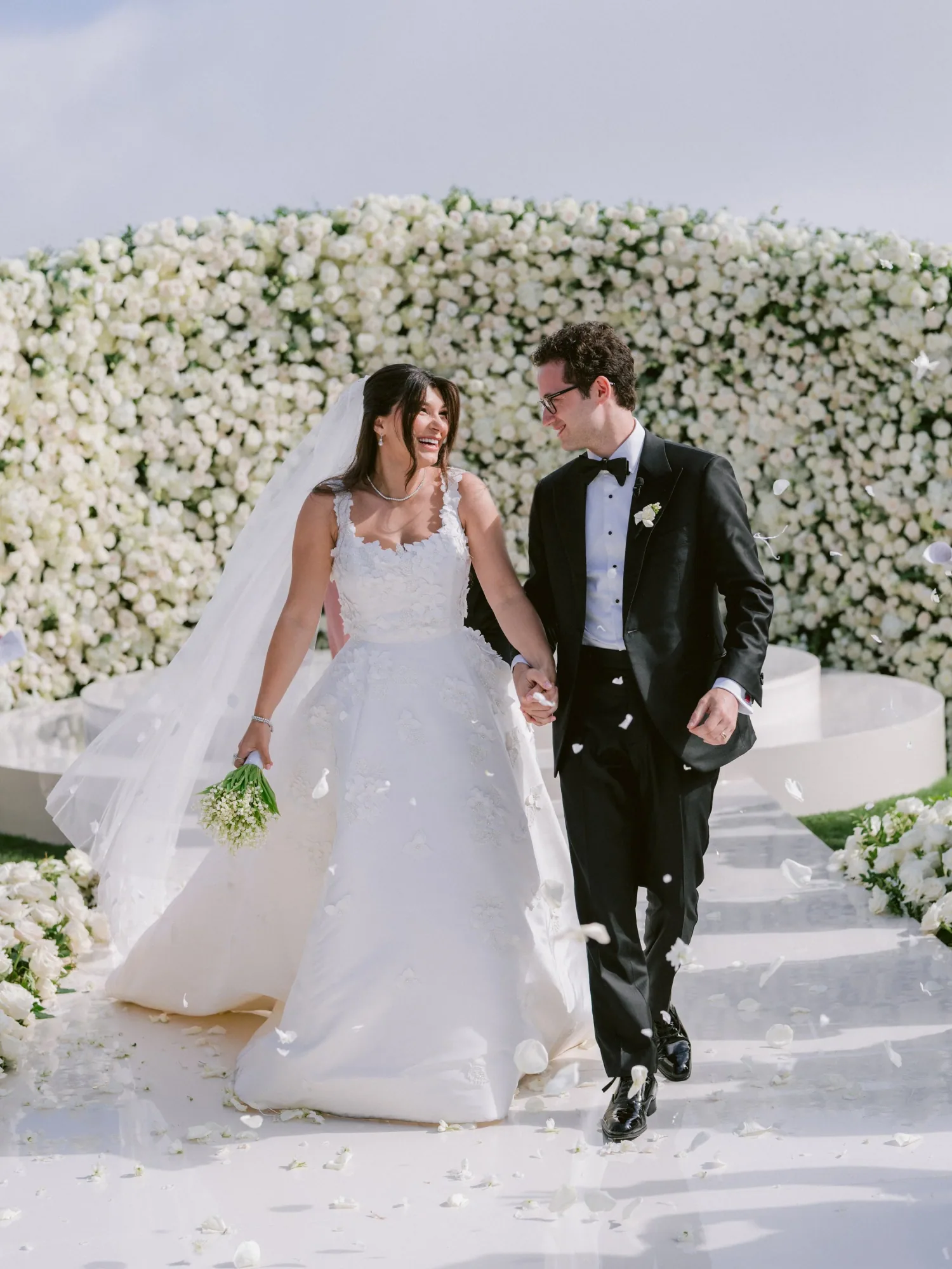 A couple walking through a white floral ceremony setting at Rosewood Miramar Beach.